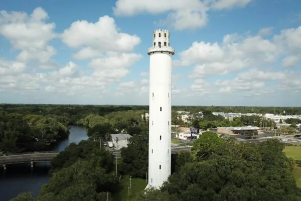 white concrete tower near green trees under white clouds and blue sky during daytime